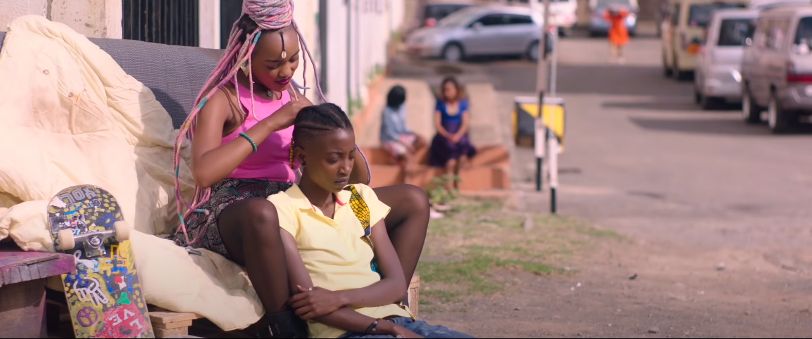 girl getting her hair braided by another girl with big dreadlocks