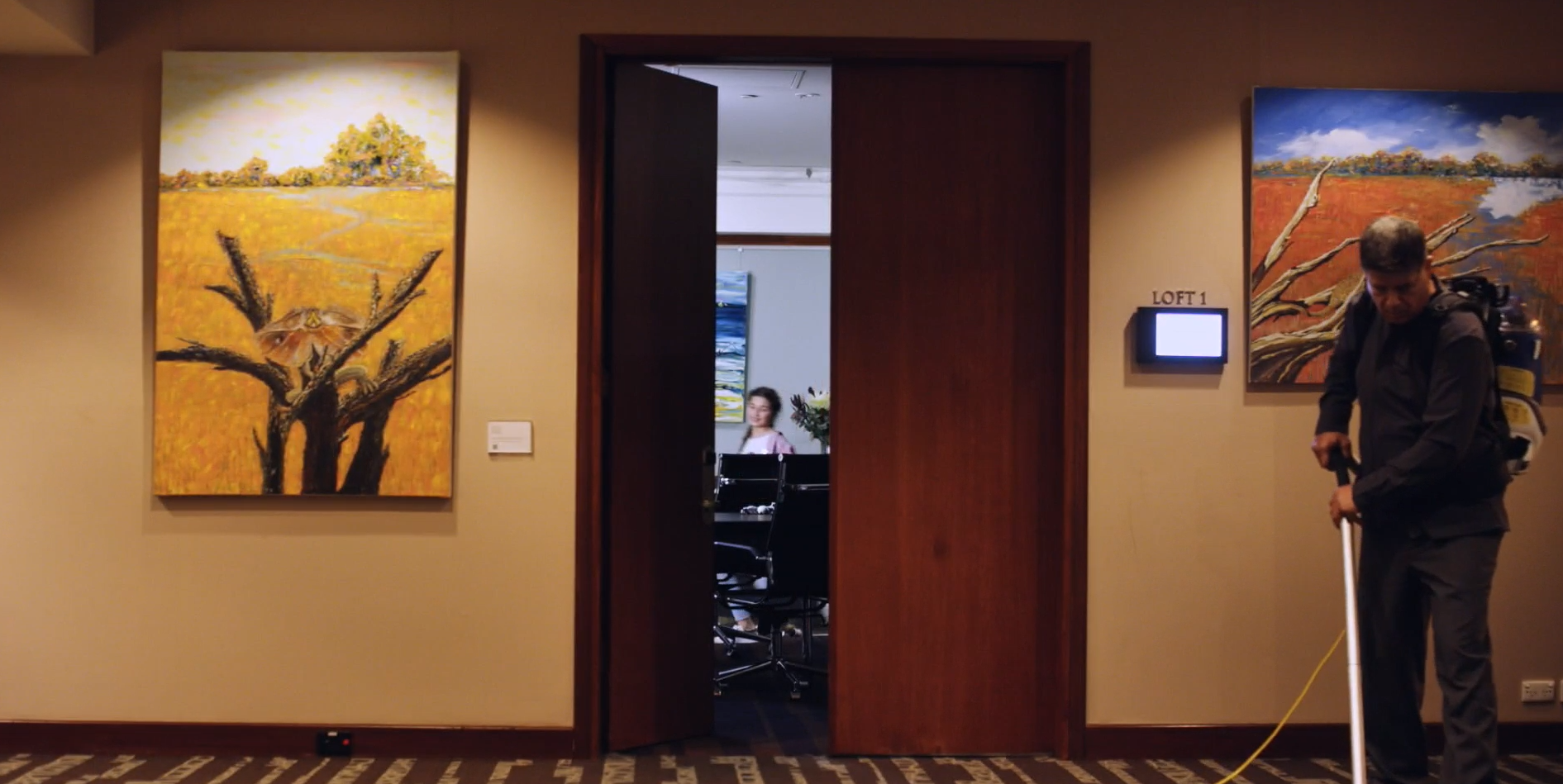 a man cleans a hallway as a young girl dances in a board room